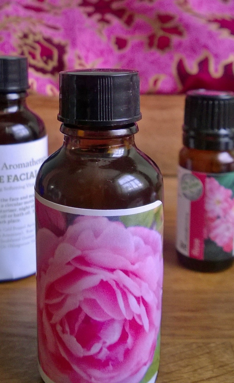 Close-up of an amber glass bottle of rose facial oil with a hand-made rose label, a pink patterned cloth behind